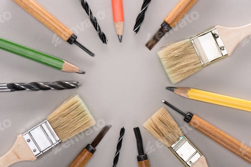 Preview: top view of various paint brushes, pencils, chisels and drills on grey