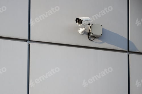 Preview: White surveillance camera built into the metal wall of the office building