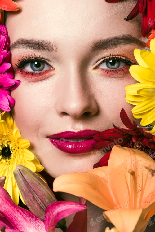 Preview: close-up portrait of beautiful young woman surrounded with various flowers looking at camera