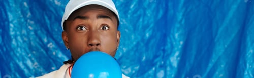 Preview: Charming young man having fun with a blue balloon against a vibrant blue backdrop