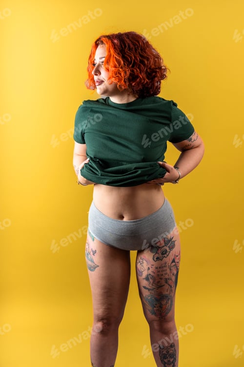 Preview: Modern tattooed non-binary redhead girl takes off her t-shirt.