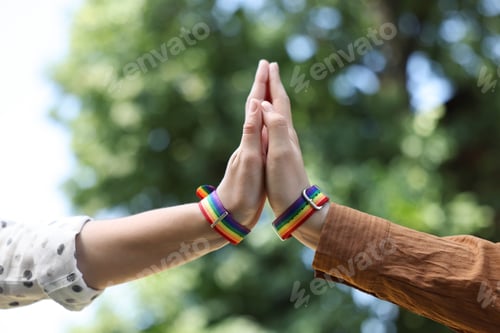 Preview: LGBT concept. Women in rainbow wristbands holding hands outdoors, closeup
