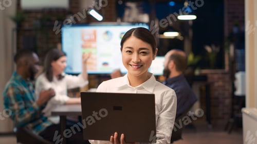 Preview: Asian businesswoman working on laptop, looking at camera, smiling