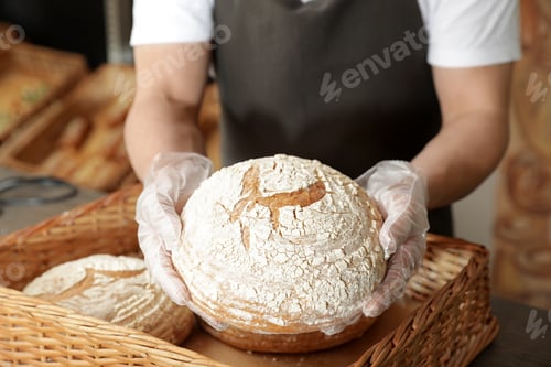 Preview: Professional baker holding loaf of bread over tray in store, closeup