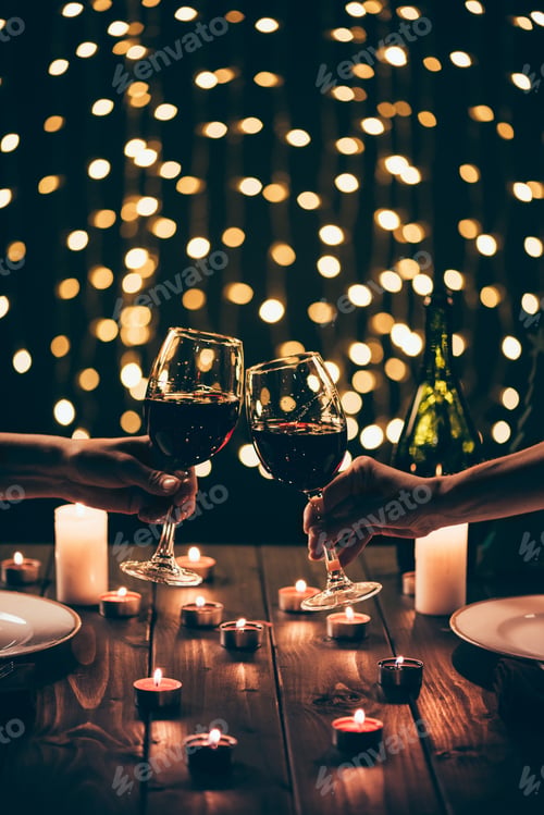 Preview: Cropped shot of two women clinking glasses with wine over served table with lit candles