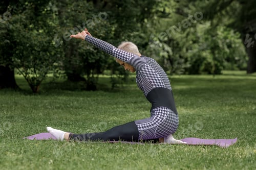 Preview: An elderly woman in sportswear does yoga on a mat outdoors.