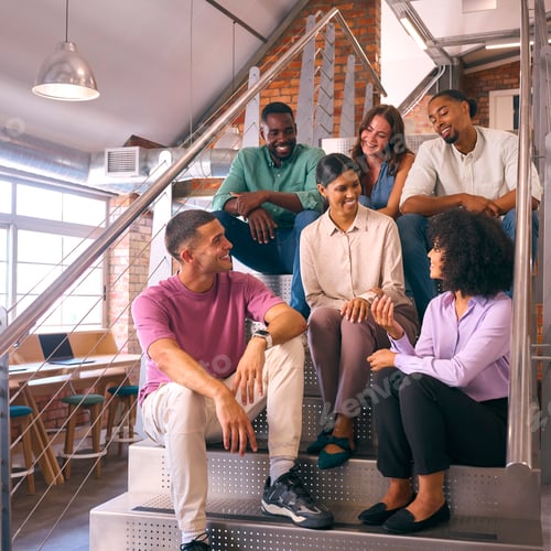 Preview: Smiling Multi-Cultural Business Team Sitting On Stairs In Modern Open Plan Office