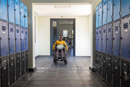 Preview: African teenage male sitting in wheelchair in school corridor with backpack and metal lockers
