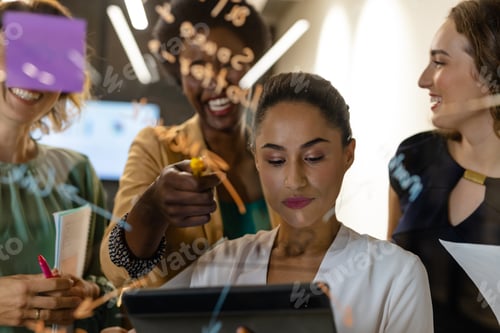 Preview: Diverse creative female colleagues in discussion brainstorming making notes on glass wall in office
