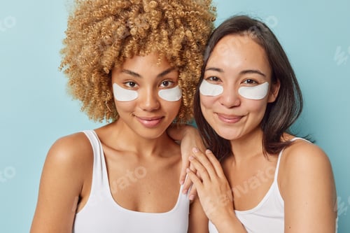 Preview: Horizontal shot of pleased young female friends wear white collagen patches under eyes take care of