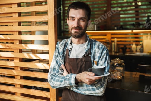 Preview: Portrait of kind barista man holding cup of coffee while working