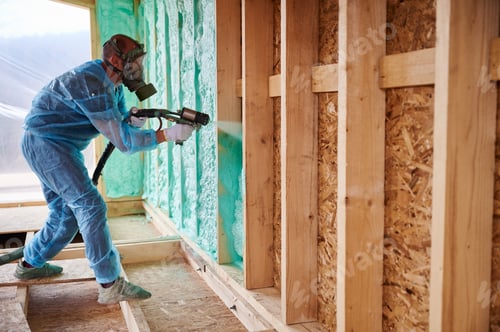 Arbeiter sprühen Polyurethanschaum zur Isolierung des Holzrahmenhauses.