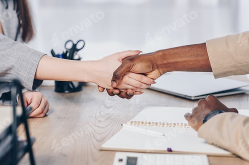 Preview: Cropped view of african american recruiter shaking hands with employee above table in office