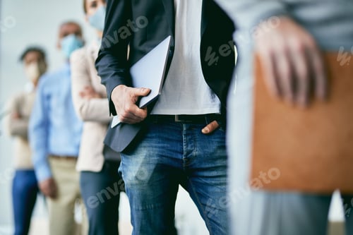 Preview: Unrecognizable businessman holding laptop while waiting in line at office building hallway.