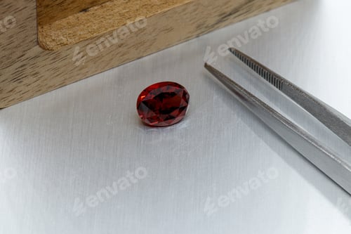 Preview: macro mineral faceted stone Garnet with tweezers on a gray background