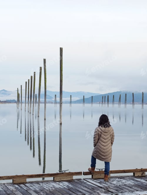 Preview: Woman enjoys the view of wood pilings in calm water.