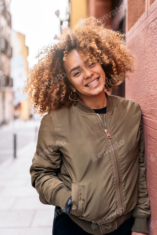 Preview: Smiling Woman with Curly Hair Leaning on Wall
