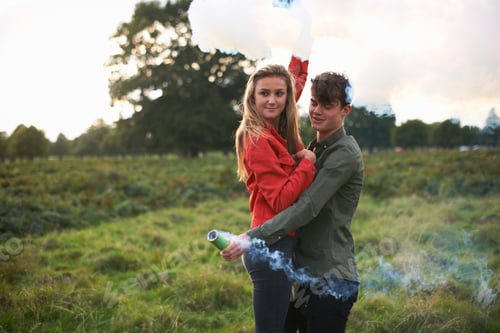 Preview: Young couple letting off smoke flares in field