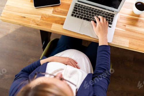 Preview: Top view of pregnant woman doing office work using laptop tablet and smartphone