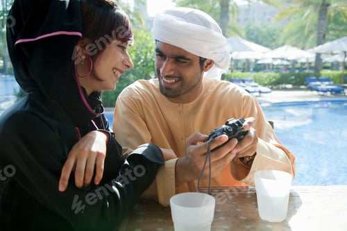 Preview: Two friends share a joyful moment playing video games together by the poolside.