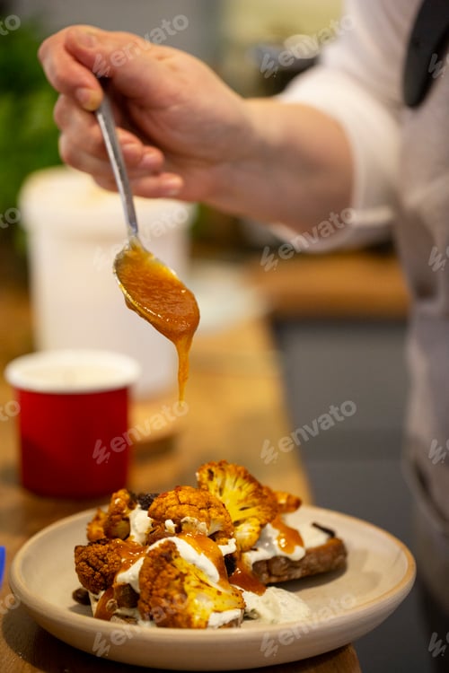 Preview: Person drizzling mango chutney onto roasted cauliflower in a cafe.