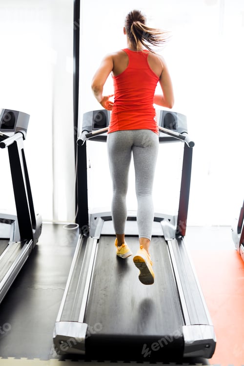 Preview: Beautiful young woman running on a treadmill in gym