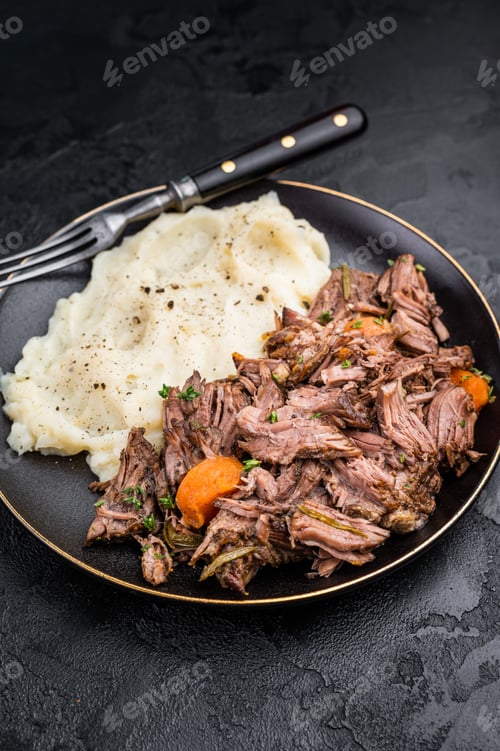 Preview: Beef stew with mashed potatoes, carrots and herbs on a plate isolated. black background. top view
