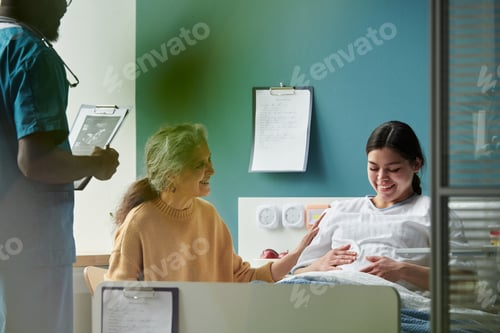 Preview: Senior Woman Comforting Young Pregnant Daughter Resting in Hospital Bed