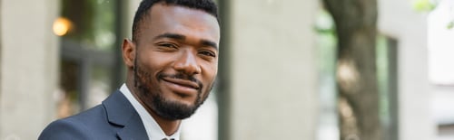 Preview: smiling african american businessman in suit looking at camera outside, banner