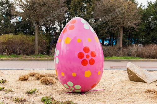 Preview: A large pink egg with colorful flower patterns is placed on a sandy area in the garden.