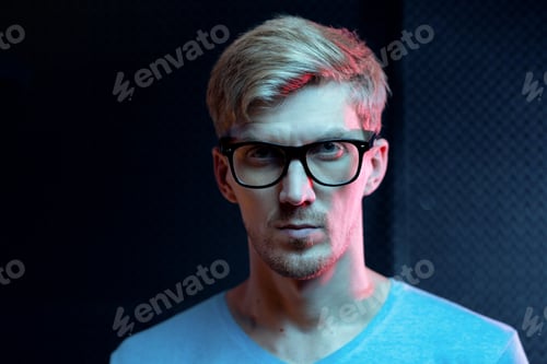 Preview: Serious young blond man of Caucasian ethnicity looking at you through eyeglasses