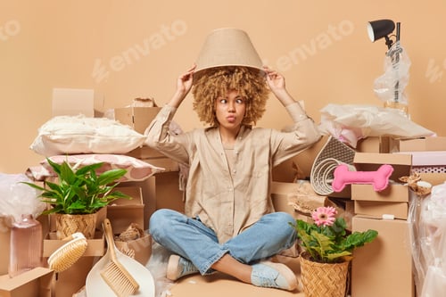 Preview: Funny woman with curly hair makes grimace sits crossed legs keeps lampshades under head moves in new