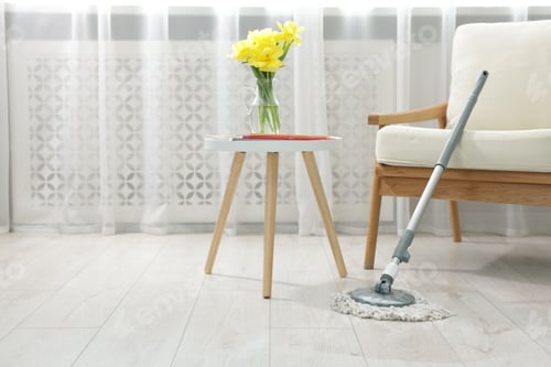Preview: String mop on floor near armchair and side table with flowers indoors, space for text
