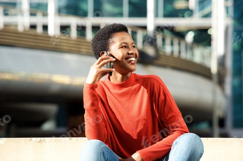 Preview: young smiling black woman talking on cellphone in city