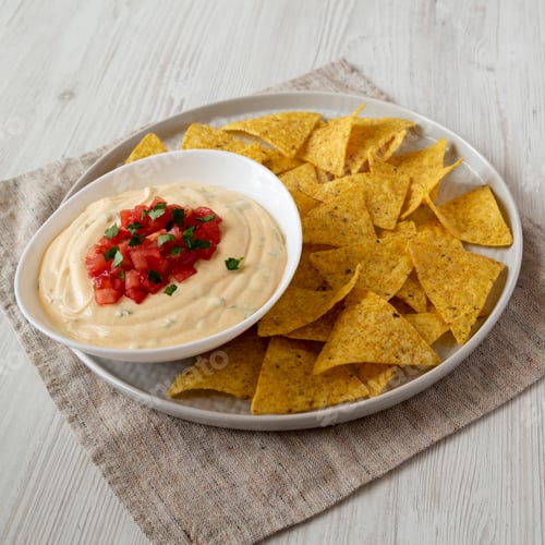 Preview: Homemade cheesy dip in a bowl, yellow tortilla chips, low angle view. Closeup.