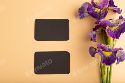 Preview: Black business card with lilac iris flowers on orange pastel background. top view, copy space.