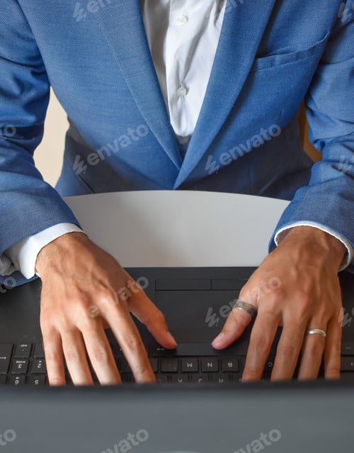 Preview: Selective focus shot of a young businessman in a blue tuxedo working on his laptop