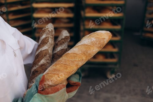 Preview: Close up of baker is taking off from oven the french baguette bread with wood peel at baking