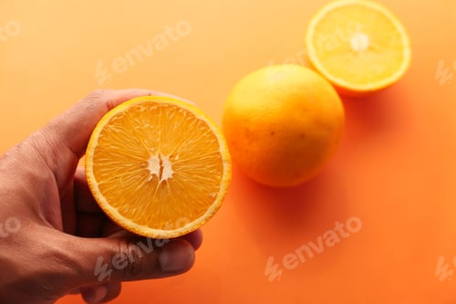 Preview: man hand holding slice of orange fruit i against blue background