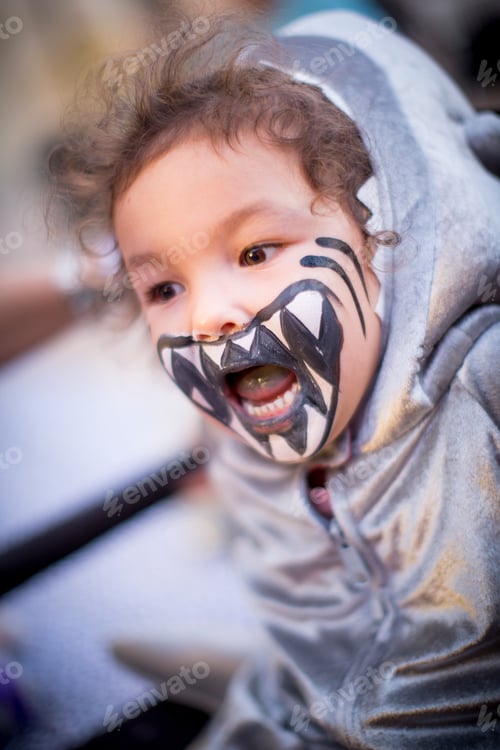 Preview: Angled view of girl dressed as shark, teeth painted on face, mouth open looking away