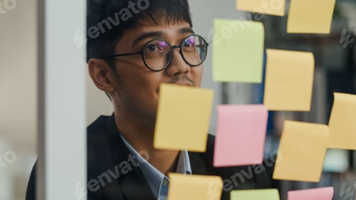 Preview: Asian creative man stick a sticky note on glass board.
