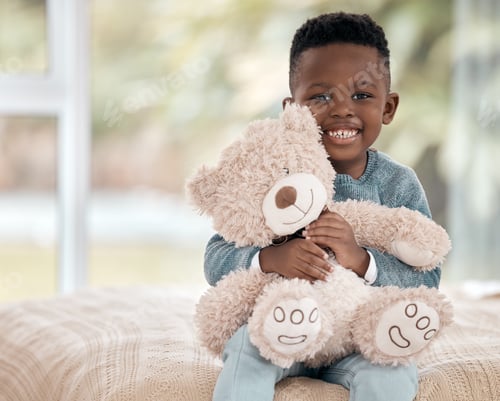 Preview: Cropped portrait of an adorable little boy sitting on a bed at home with his teddy bear