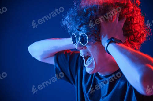 Preview: Vintage style glasses. Young man with curly hair is indoors illuminated by neon lighting