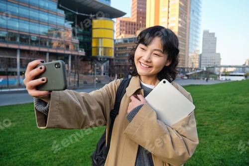 Preview: Happy university student, korean girl takes selfie with her papers and digital tablet, holds