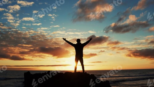 Preview: Man stands on a rock against the ocean during summer sunset.