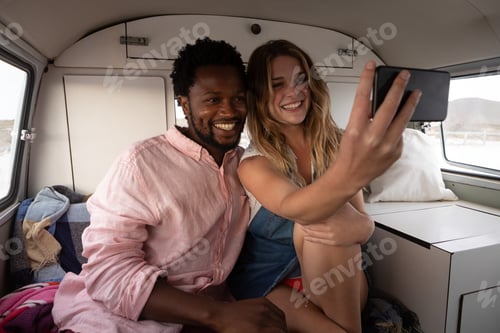 Preview: Front view of a multi-ethnic couple taking a selfie in camper van at beach