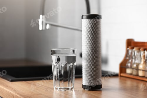 Preview: A glass of clean fresh water and carbon filter cartridge on wooden table in a kitchen interior.