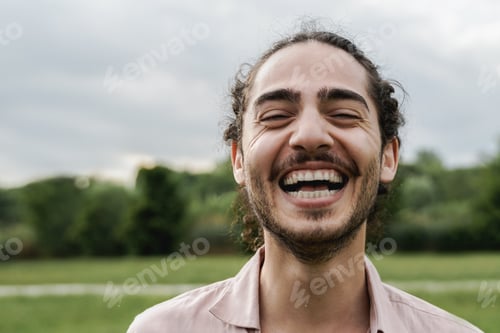 Preview: Young happy man smiling and looking at camera outdoor at city park - Focus on eyes