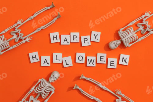 Preview: Happy Halloween word on wooden texture scrabble letters with skeletons on orange background