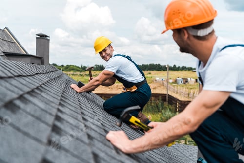 Preview: selective focus of happy repairman looking at coworker on roof